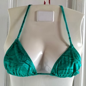 May include: A teal green bikini top with adjustable straps. The top is made of a silky material and has a triangle shape.