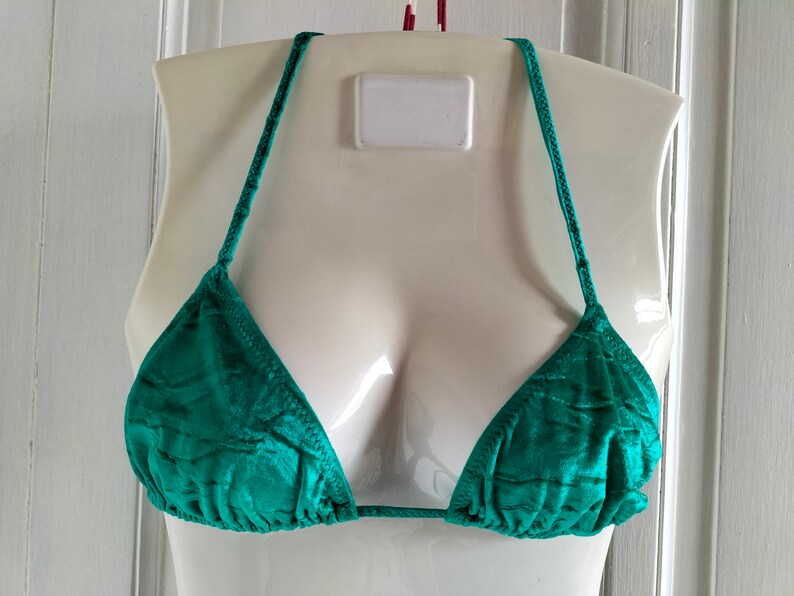 May include: A teal green bikini top with adjustable straps. The top is made of a silky material and has a triangle shape.
