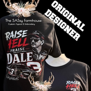 May include: A black t-shirt featuring a graphic of Dale Earnhardt with the text "RAISE HELL PRAISE DALE" and the number 3. The design includes a race car, a portrait of the driver, and floral antler accents. The text "The SASsy Farmhouse" is printed below.