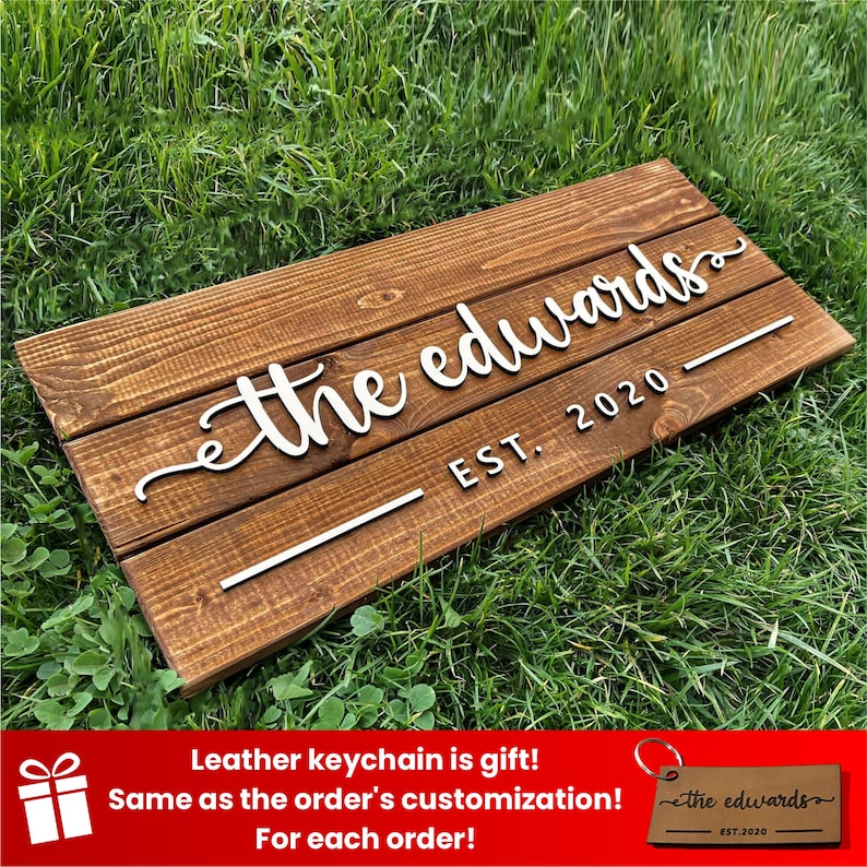 May include: A wooden sign with the text "the edwards EST. 2020" in white raised letters. The sign is on a green grassy surface.