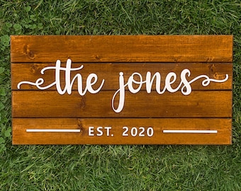 May include: A wooden sign with the text "the jones" in white cursive lettering and "EST. 2020" below it.