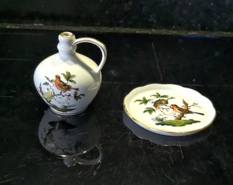 May include: A white porcelain pitcher with a gold rim and a bird design. The pitcher has a handle and a spout. A matching white porcelain plate with a gold rim and a bird design is also shown.