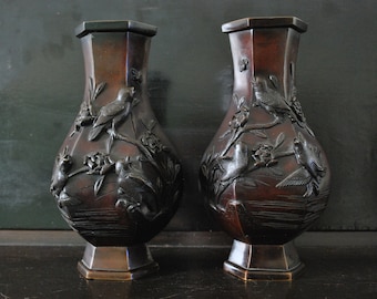 May include: Two dark brown ceramic vases with intricate bird and floral designs. The vases have a rounded body and a wide mouth.