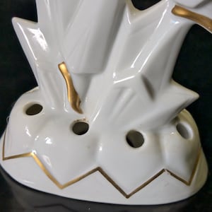 May include: White ceramic flower frog with a gold trim. The frog has a geometric design and multiple holes for holding flowers.