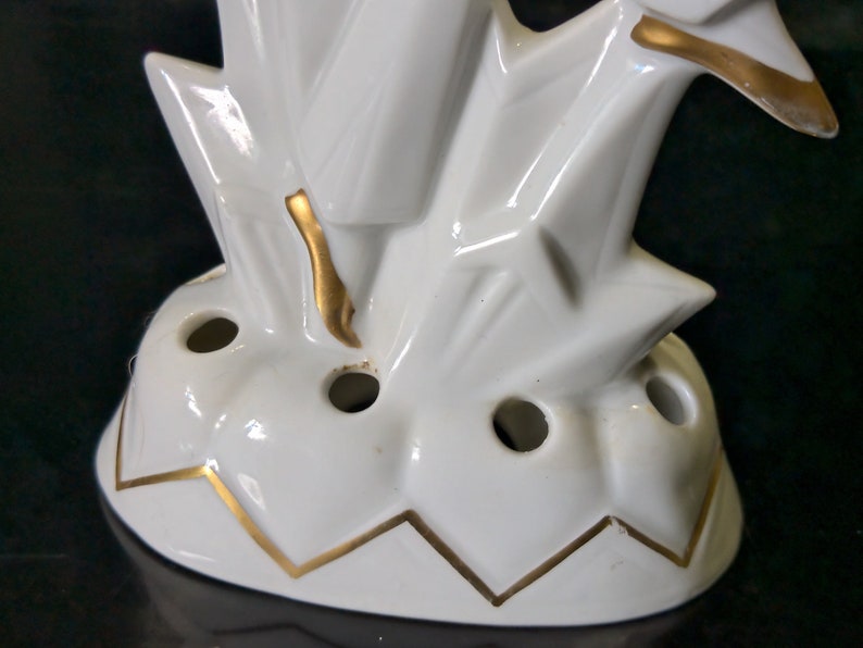May include: White ceramic flower frog with a gold trim. The frog has a geometric design and multiple holes for holding flowers.