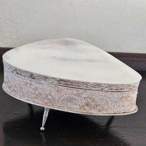 May include: White ceramic heart-shaped trinket box with a lace trim and three silver legs.