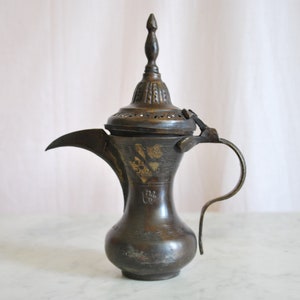 May include: A vintage brass teapot with a decorative lid and a curved spout. The teapot has intricate floral designs and is in a dark brown color.
