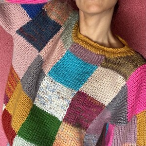May include: A patchwork sweater in a variety of colors including pink, blue, green, and yellow. The sweater has a crew neck and long sleeves. The design is made of squares of different colored yarn.
