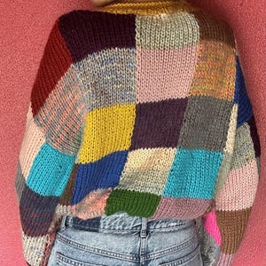 May include: A patchwork sweater in a variety of colors, including red, yellow, blue, and pink. The sweater has a round neckline and long sleeves. The sweater is made of a chunky knit material.