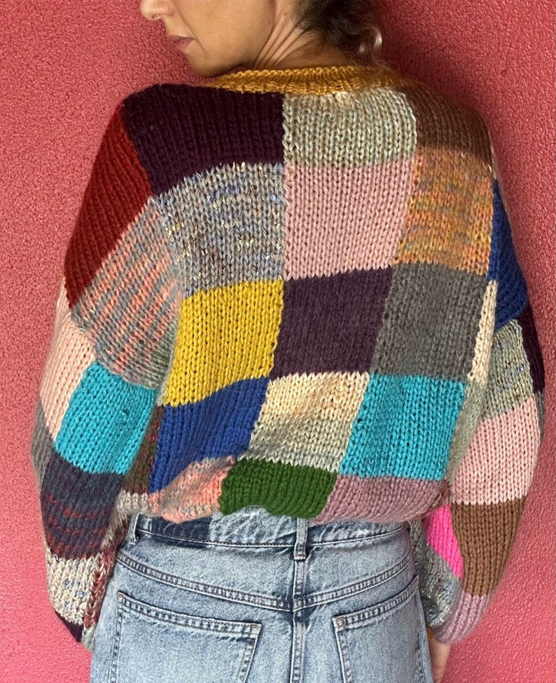 May include: A patchwork sweater in a variety of colors, including red, yellow, blue, and pink. The sweater has a round neckline and long sleeves. The sweater is made of a chunky knit material.