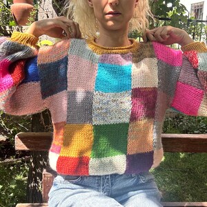 May include: A colorful patchwork sweater with a round neckline and long sleeves. The sweater features a variety of colors, including pink, blue, green, and yellow. The sweater is made of a knitted material and is a cozy garment.