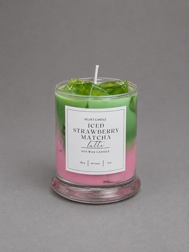 May include: A soy wax candle in a clear glass jar featuring a layered pink and green design topped with green wax ice cubes. The white label reads VELVET CANDLE ICED STRAWBERRY MATCHA latte SOY WAX CANDLE 180 g | 40 hours | 8 oz with a central wick.