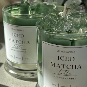 Puede incluir: Dos velas de cera de soja en vasos de vidrio transparentes con etiquetas blancas que dicen "Velvet Candle Iced Matcha Latte Soy Wax Candle". Las velas tienen un aroma a latte matcha helado verde. La vela de la izquierda tiene un tamaño de 12 oz y la vela de la derecha tiene un tamaño de 250 g.
