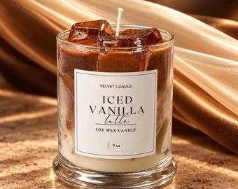 May include: A soy wax candle in a clear glass jar featuring a layered brown and white appearance resembling an iced coffee drink. The top includes brown wax cubes and a single white wick. A white label reads VELVET CANDLE ICED VANILLA LATTE 9 oz.