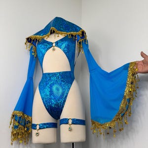 Puede incluir: Un body azul con un diseño recortado, combinado con mangas y capucha a juego. El conjunto está adornado con ribetes dorados y detalles en forma de estrella, e incluye ligas con abalorios decorativos. El conjunto se exhibe en un maniquí.