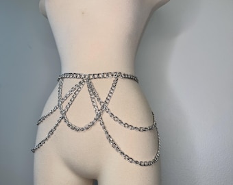 May include: Silver chain belt with multiple strands hanging down. The belt is draped on a mannequin. The chain links are small and closely linked together. The belt is a shiny silver color.