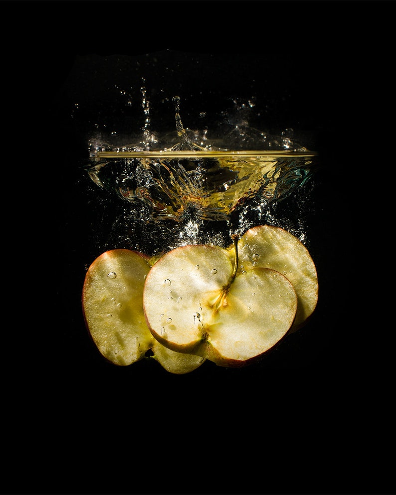 Peut inclure: Trois tranches de pomme rouge tombant dans l'eau, cr&eacute;ant des &eacute;claboussures. Les tranches de pomme sont immerg&eacute;es dans l'eau, la tranche sup&eacute;rieure &eacute;tant partiellement hors de l'eau. L'arri&egrave;re-plan est noir.