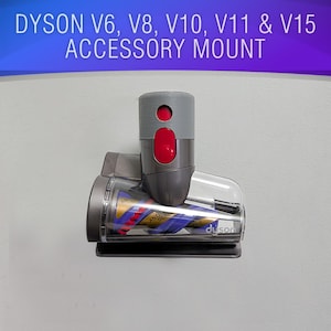 May include: A gray Dyson accessory mount for V6, V8, V10, V11, and V15 models. The mount features a red button and a clear plastic component with the brand name "duson" visible. The text "DYSON V6, V8, V10, V11 & V15 ACCESSORY MOUNT" is displayed.
