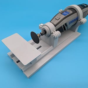 May include: A gray rotary tool with a black cutting disc is mounted on a gray stand with an adjustable work surface. The tool is gray and black with a blue power button. The background is a solid blue.