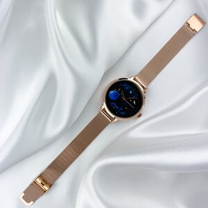May include: A rose gold mesh band watch with a round face featuring a blue and black galaxy design.