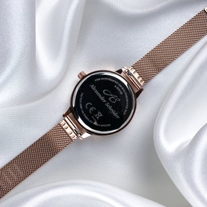 May include: The back of a rose gold watch with a black face. The watch face has the text "Alexander Schr&ouml;der" and "8 bar water resistant" printed on it.