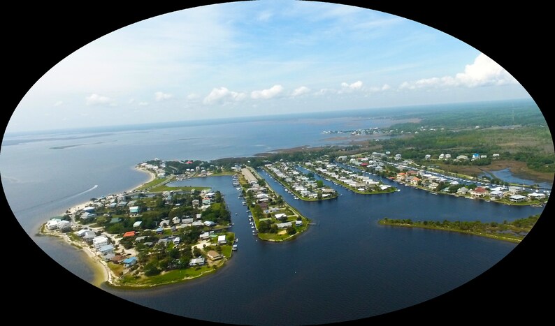 Puede incluir: Vista a&eacute;rea de una comunidad costera con casas, muelles y barcos. La imagen muestra una pen&iacute;nsula con una v&iacute;a fluvial y una masa de agua bajo un cielo azul con nubes. La escena es un d&iacute;a soleado.