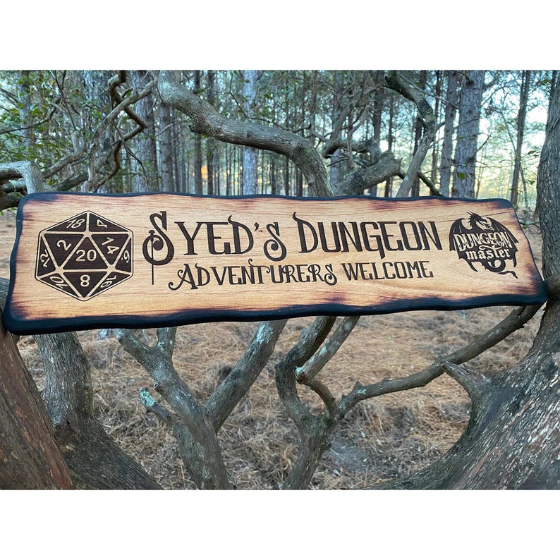 以下が含まれることがあります： 焦げ付いた縁のある木製の看板で、20面ダイス、"SYED'S DUNGEON ADVENTURERS WELCOME"というテキスト、そして"DUNGEON MASTER"というテキストの入ったドラゴンが描かれている。