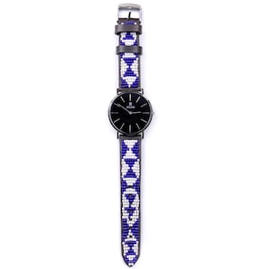 May include: A black watch with a white and blue beaded band. The watch face is black with white hands and a white logo that says "JAAK" in the centre.