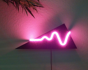 May include: A pink neon light shaped like a wavy line is mounted on a black triangular piece of wood. The light is casting a pink glow on the wall behind it.