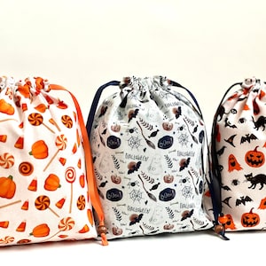 May include: Three Halloween-themed drawstring bags with different patterns. The first bag has a white background with orange pumpkins, candy canes, and candy corn. The second bag has a white background with black bats, pumpkins, ghosts, and the words "Boo!" and "Halloween". The third bag has a white background with black bats, pumpkins, ghosts, and black cats.