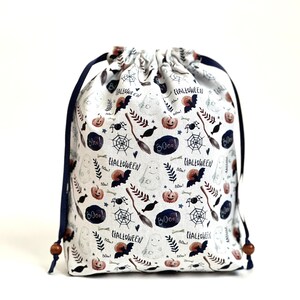 May include: White drawstring bag with a Halloween themed print. The print features bats, pumpkins, ghosts, spiders, bones, and the words "Boo!" and "Halloween".
