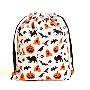 May include: A white drawstring bag with a Halloween print featuring orange pumpkins, black cats, bats, ghosts, and crows. The bag has black drawstrings with orange beads.