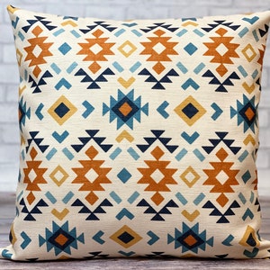 May include: A square throw pillow with a geometric pattern in shades of blue, orange, yellow, and black on a cream background.