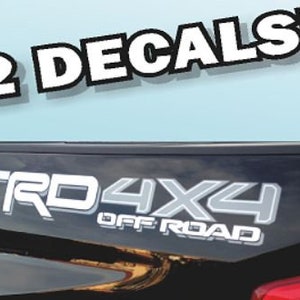 Op de afbeelding: Twee witte en grijze vinyl stickers met de tekst "TRD 4X4 OFF ROAD".