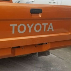 May include: A close-up of the back of an orange pickup truck with the word "TOYOTA" in white letters on the tailgate.