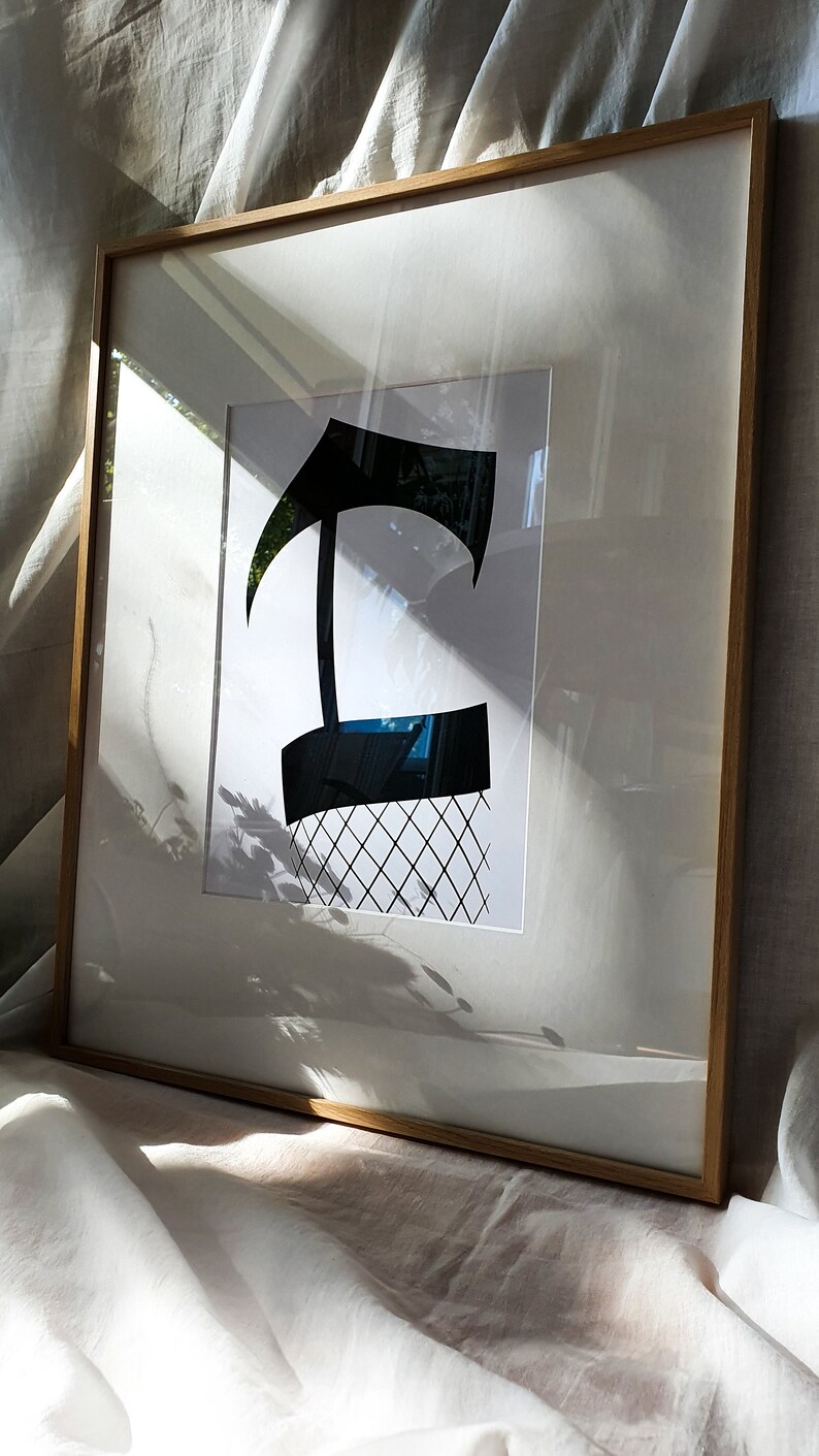 May include: A framed black and white print of a stylized letter 'T' with a grid pattern underneath. The print is in a light wood frame.