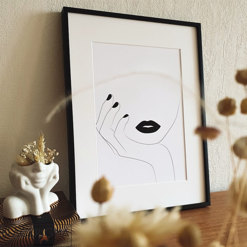May include: Black and white line art print of a woman's face with bold black lips. The woman's hand is resting on her chin. The print is framed in a black frame.