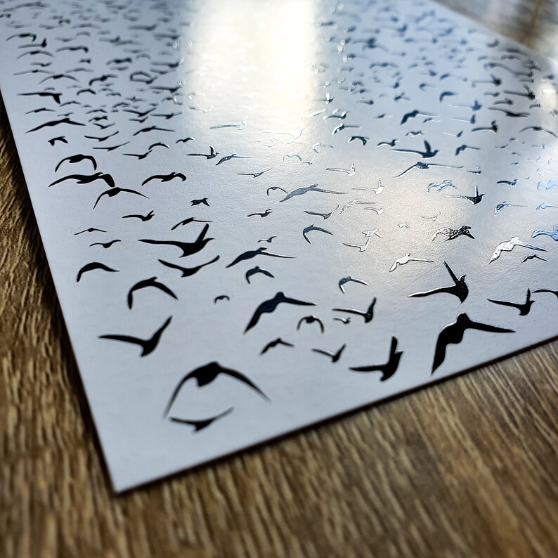 K&ouml;nnte beinhalten: Ein wei&szlig;es Blatt Papier mit schwarzen Silhouetten von V&ouml;geln darauf gedruckt. Die V&ouml;gel sind in einem zuf&auml;lligen Muster angeordnet, wobei sich einige V&ouml;gel &uuml;berlappen. Das Papier ist leicht zerknittert und hat einen leichten Glanz.