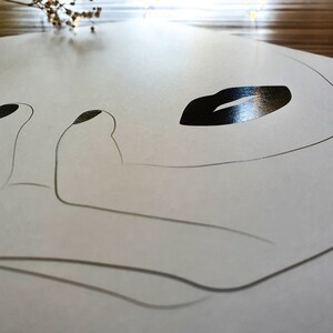 May include: A white paper placemat with a black line drawing of a face with a closed eye and a large, black, glossy lip.