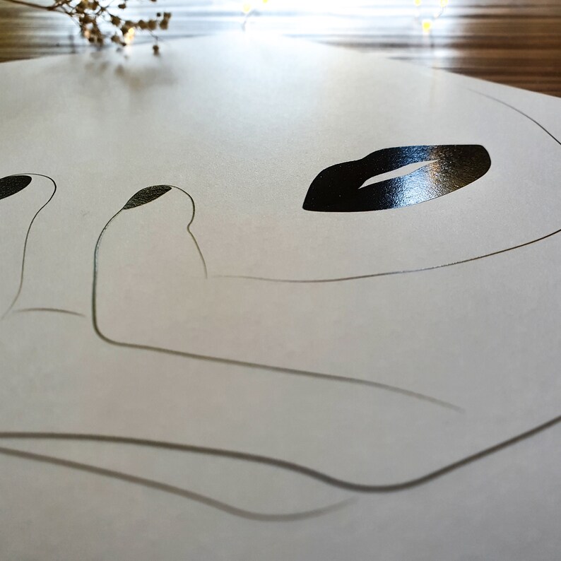 May include: A white paper placemat with a black line drawing of a face with a closed eye and a large, black, glossy lip.