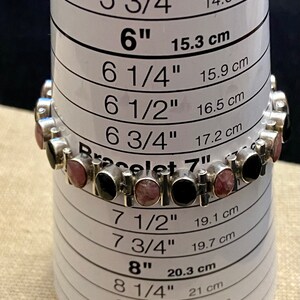 May include: A silver bracelet with black and pink stones, measured against a sizing chart. The bracelet is 7 inches in length.