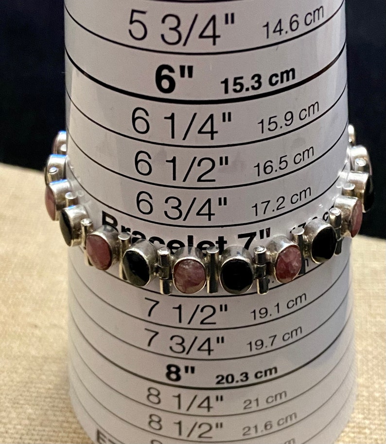 May include: A silver bracelet with black and pink stones, measured against a sizing chart. The bracelet is 7 inches in length.