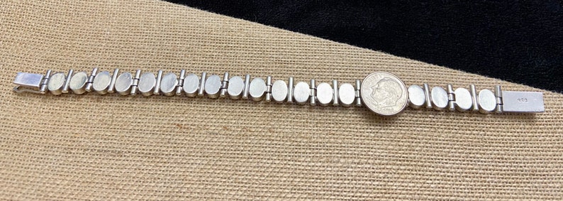 May include: Silver bracelet with oval-shaped white mother-of-pearl links. The bracelet has a clasp and a tag that says "925".
