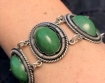 Könnte beinhalten: Ein silbernes Armband mit drei ovalen grünen Steinen, die in verzierten Silberrahmen gefasst sind. Das Armband hat ein Kettenglieddesign.