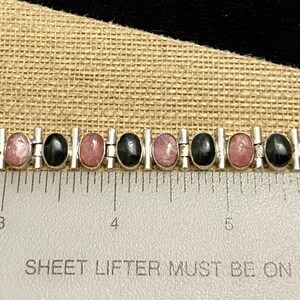May include: A silver bracelet with alternating black and pink oval stones. The bracelet is 7 inches long.