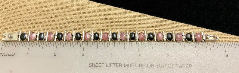 May include: A silver bracelet with alternating black and pink oval stones. The bracelet is 7 inches long.