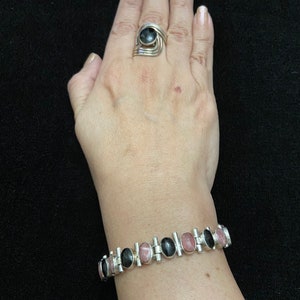 May include: A silver bracelet with alternating black and pink oval stones. The bracelet is made of linked metal bars with a polished finish.