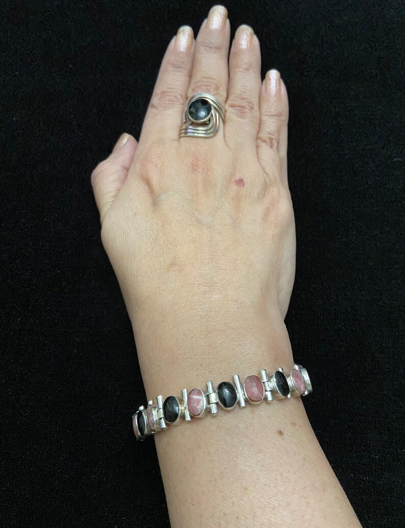 May include: A silver bracelet with alternating black and pink oval stones. The bracelet is made of linked metal bars with a polished finish.