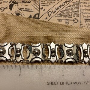May include: Silver-toned bracelet with a geometric design. The bracelet features square and oval links with circular and beaded accents. The bracelet is approximately 6 inches long.