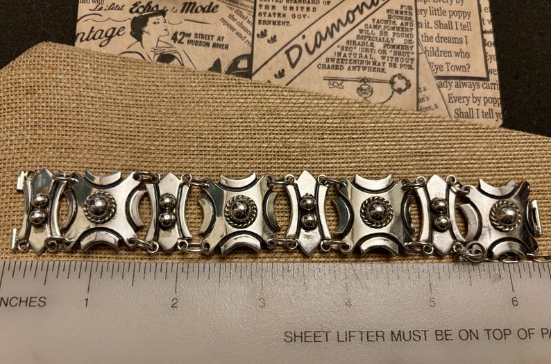 May include: Silver-toned bracelet with a geometric design. The bracelet features square and oval links with circular and beaded accents. The bracelet is approximately 6 inches long.